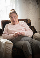 An old woman in glasses sitting in the armchair and knitting. Looking judgingly at somebody