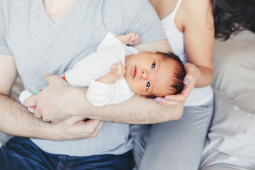 Parents mother and father holding in hands Chinese mixed race infant son daughter. Closeup portrait of Asian newborn baby. Home lifestyle authentic natural moment.