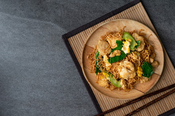 Fried dry instant noodle with chicken and chinese kale in wooden dish on concrete table.