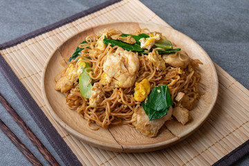 Fried dry instant noodle with chicken and chinese kale in wooden dish on concrete table.
