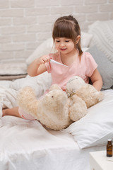 cute child girl playing doctor with teddy bear at home.