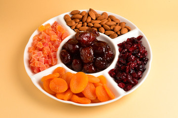 Mix of dried fruits and nuts on a white plate. Apricot, almond, raisin, dates fruit. On a brown background. Space for text or design.