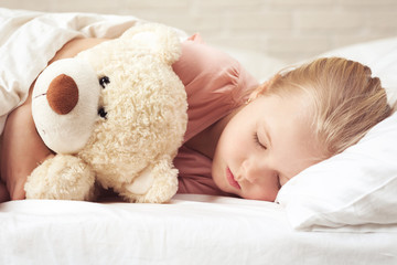 Cute little child girl sleeping with teddy bear in her bed