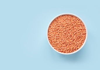 Raw red lentils in a white bowl on a blue background. Top view, copy space, minimalistic.