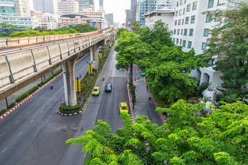 Cityscape view of a few car on the road along rail track with many tree