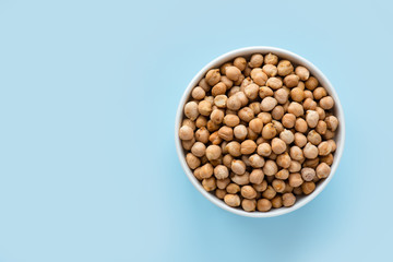 Raw chickpeas in a white bowl on a blue background. Top view, copy space, minimalistic.