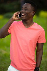African american man in living coral t-shirt talking by smartphone at summer day