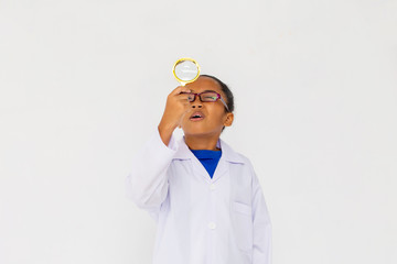 Young preteen African American kid wearing lab coat looking up with magnifier in white isolated background. Can be doctor or scientist.