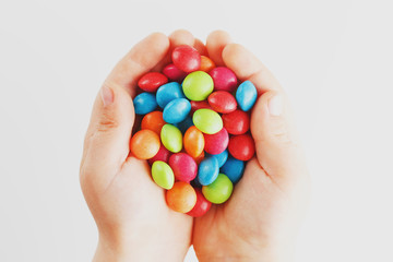 Multicolored candies in the hands of a child on a white isolated background. Low contrast