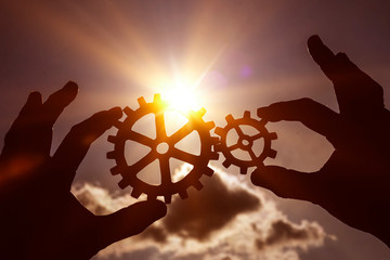 two gears in the hands of people at sunset. the mechanism of interaction.