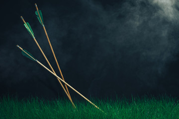 Three wooden arrows in the grass. Beautiful smog background. Medieval weapons handmade.