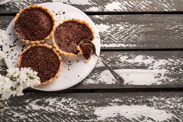 chocolate tartlets on a white plate, white lilac, old wooden rustic backdrop, copy space