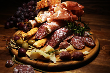 antipasto various appetizer. Cutting board with prosciutto, salami, cheese, bread and olives on dark wooden background