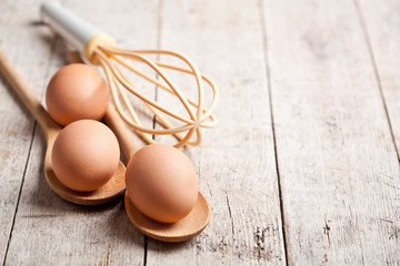 Chicken eggs and kitchen utensil on rustic wooden table background.