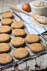 Baking grid with fresh oat cookies on rustic wooden table background, ingredients and kitchen utensil closeup on rustic wooden table.