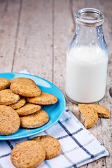 Fresh baked oat cookies on blue ceramic plate on linen napkin and bottle of milk on rustic wooden table.