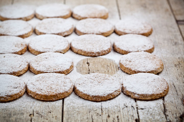 Fresh baked oat cookies with sugar powder on rustic wooden table.