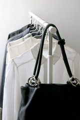 Minimal capsule wardrobe on a clothes rack. Monochrome tops and black leather bag. Selective focus.