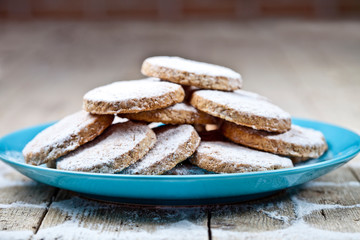 Fresh baked oat cookies with sugar powderon blue ceramic plate on rustic wooden table.