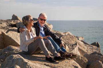 Happy senior couple sitting on rocks by the sea