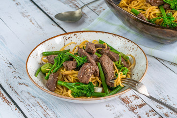 Honey and sesame beef noodles with green vegetables.