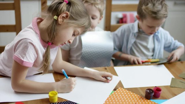 girl show to draw some cute things on paper with pen to her brothers