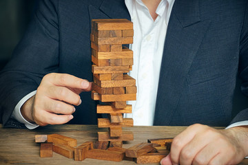Businessman try to move wood block from wood building stack,risk concept.