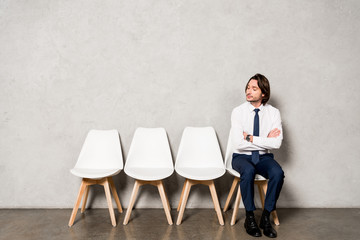 Fototapeta premium handsome man sitting on chair with crossed arms while waiting job interview