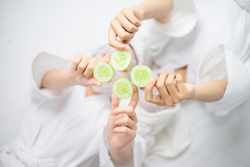 Two female in spa dress show hand holding cucumber slice in spa salon, Cucumber slice mask for treatment face skin. 