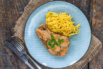 Pork chops in creamy cajun sauce with button mushrooms and egg noodles garnished with parsley - top view