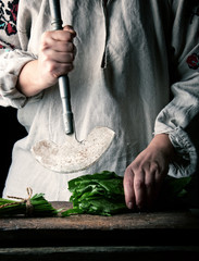 woman in a gray linen dress is cutting green leaves of fresh sorrel on a wooden cutting board