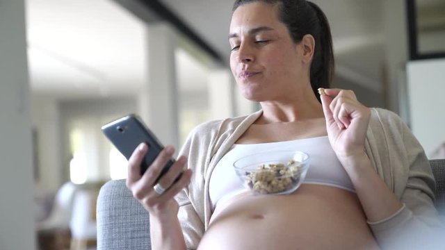 Pregnant woman in sofa, eating cereals 