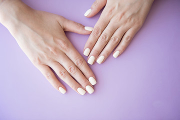 Manicured hands on purple background. Hands with manicured nails colored with beige nail polish.