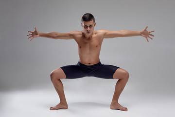 Obraz premium Photo of a handsome man ballet dancer, dressed in a black shorts, making a dance element against a gray background in studio.