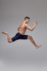 Obraz premium Photo of a handsome man ballet dancer, dressed in a black shorts, making a dance element against a gray background in studio.