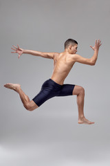 Photo of a handsome man ballet dancer, dressed in a black shorts, making a dance element against a gray background in studio.