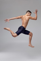 Fototapeta premium Photo of a handsome man ballet dancer, dressed in a black shorts, making a dance element against a gray background in studio.