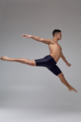 Fototapeta premium Photo of a handsome man ballet dancer, dressed in a black shorts, making a dance element against a gray background in studio.