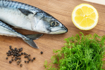 Two raw mackerels, fresh dill, black peppercorns and lemon on a brown wooden cutting board. Seafood, healthy eating and cook at home.