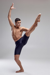 Obraz premium Photo of a handsome man ballet dancer, dressed in a black shorts, making a dance element against a gray background in studio.