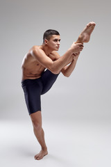 Photo of a handsome man ballet dancer, dressed in a black shorts, making a dance element against a gray background in studio.