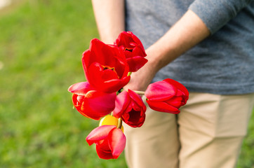 Anonymous man holding a bouquet of flowers in a park. A man on a date. Courtesy in a relationship. Bouquet for one's beloved. St. Valentine's Day present. Expressing love in a romantic relationship.