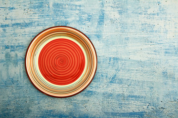 Empty red ceramic dish plate with spiral pattern on wooden white blue background. Top view with copy space.