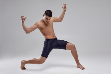 Fototapeta premium Photo of a handsome man ballet dancer, dressed in a black shorts, making a dance element against a gray background in studio.