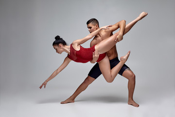 Fototapeta na wymiar The couple of an athletic modern ballet dancers are posing against a gray studio background.