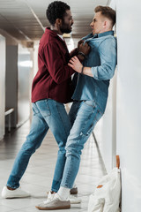 full length view of two students in jeans fighting in corridor in college