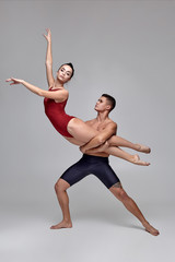 The couple of an athletic modern ballet dancers are posing against a gray studio background.