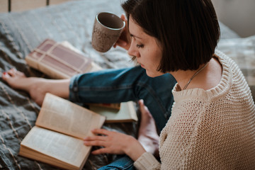 girl reading a book and drinking coffee in bed feet on the wall.