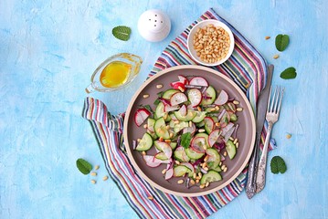Light salad of crispy radish, cucumber and mint leaves with citrus dressing on a brown plate. Sprinkled with pine nuts. Top view.
