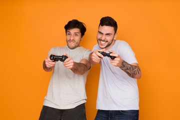 Two Friends Playing Video Games Over Orange Background © Prostock-studio
